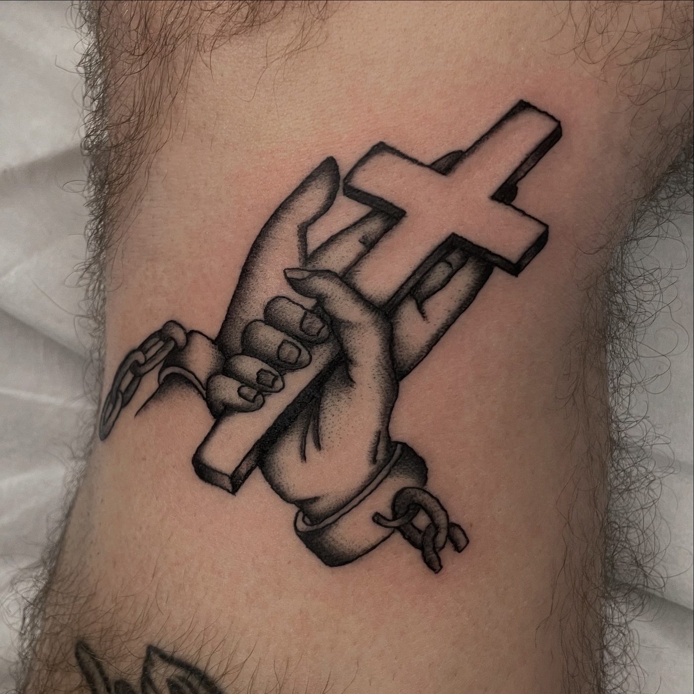 Bold black and grey tattoo of two hands with broken chains clasped around a wooden cross