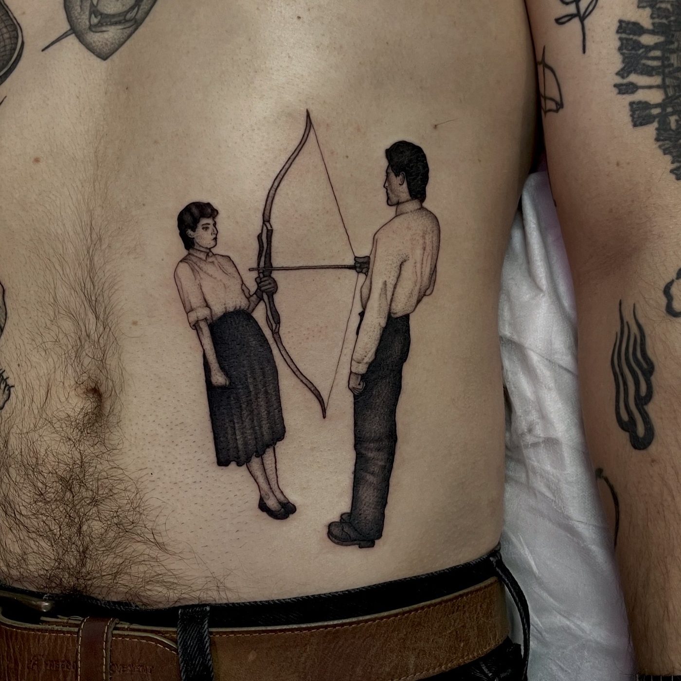 Fine-line rib tattoo of a woman and a man standing back to back drawing a single bow together