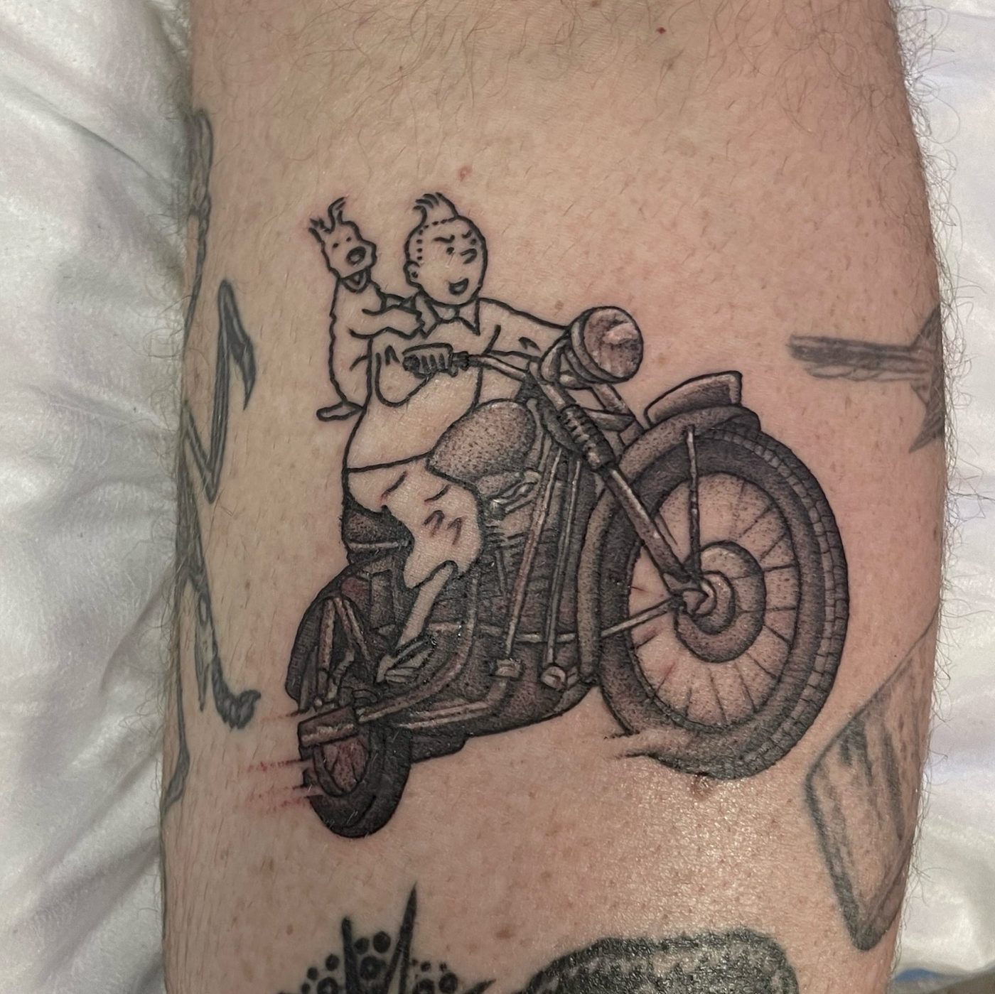 Black and grey leg tattoo of Tintin and Snowy riding a vintage motorcycle