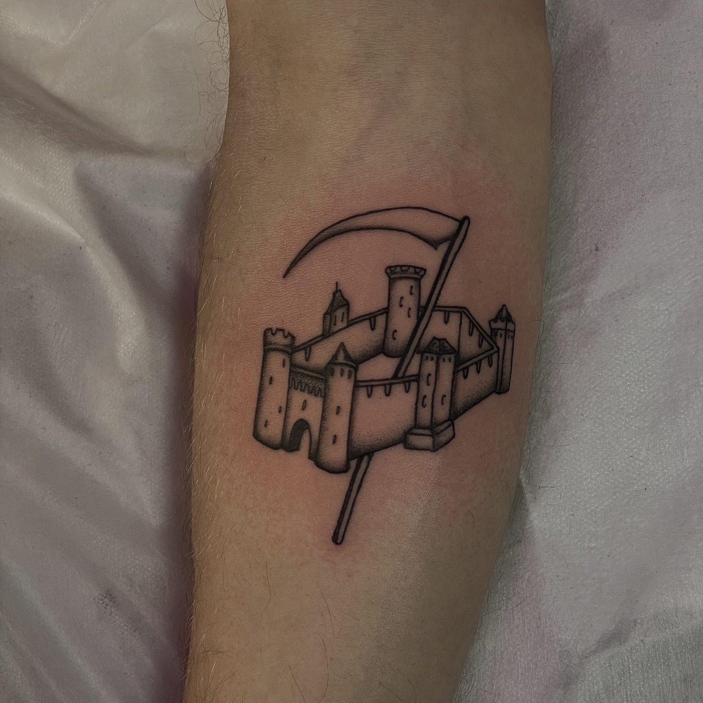 Black and grey arm tattoo of a medieval castle with a scythe sweeping behind its towers