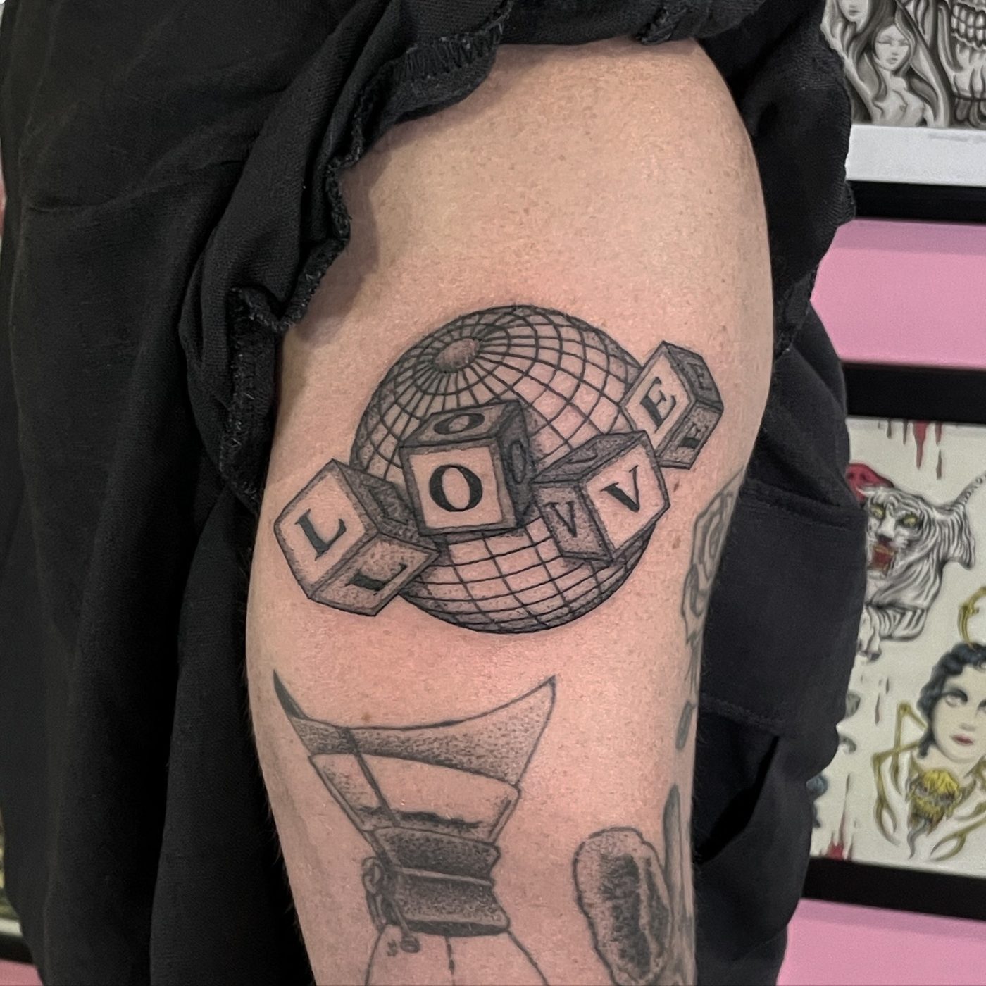 Thigh tattoo of a wire frame disco globe with alphabet blocks spelling the word LOVE