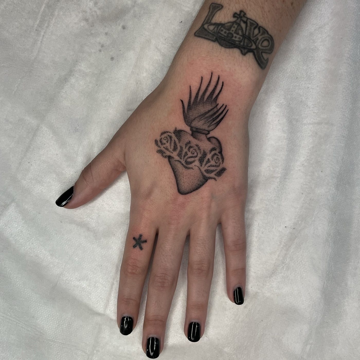 Dotwork hand tattoo of a sacred heart wrapped in roses with flames rising above