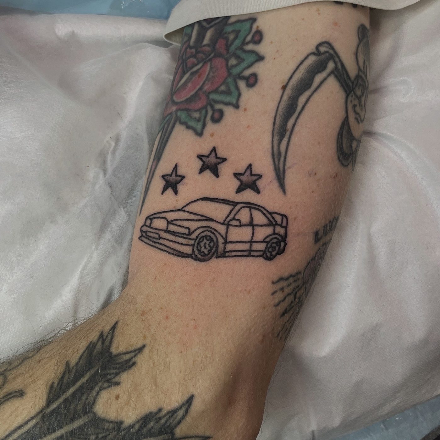 Fine-line leg tattoo of a sports car beneath three dotwork stars