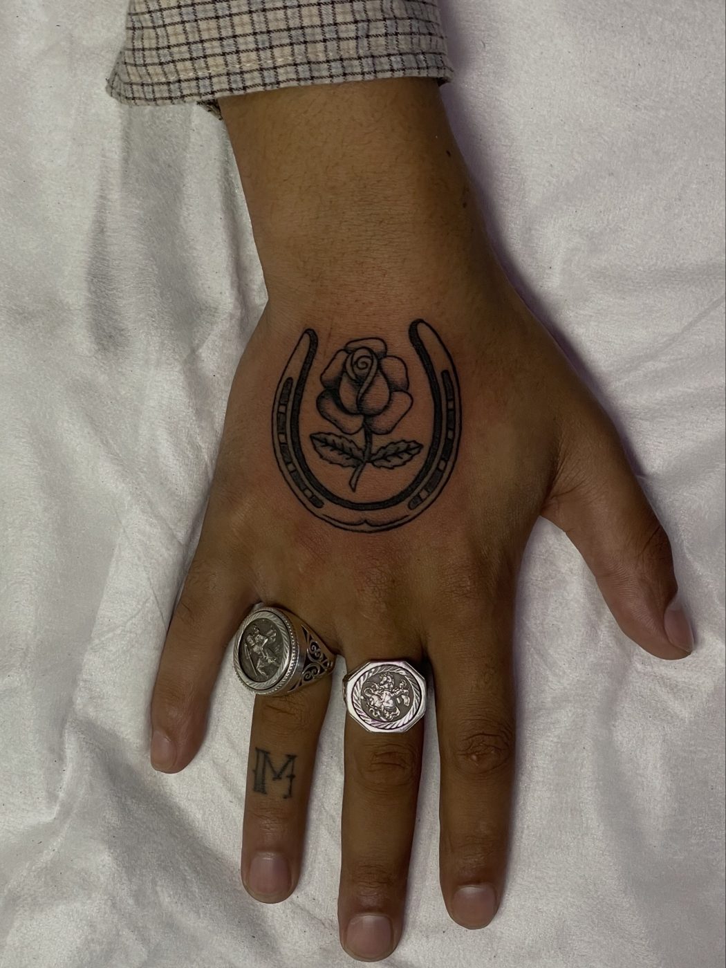 Hand tattoo of a single rose inside a horseshoe, worn with signet rings