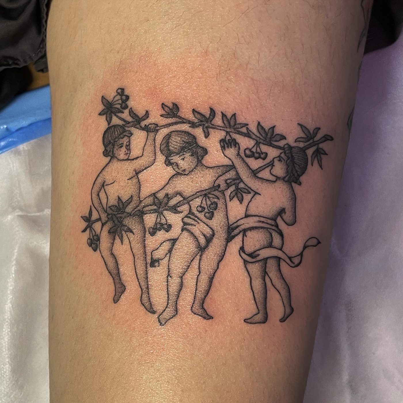 Fine-line arm tattoo of three classical figures harvesting cherries from a branch