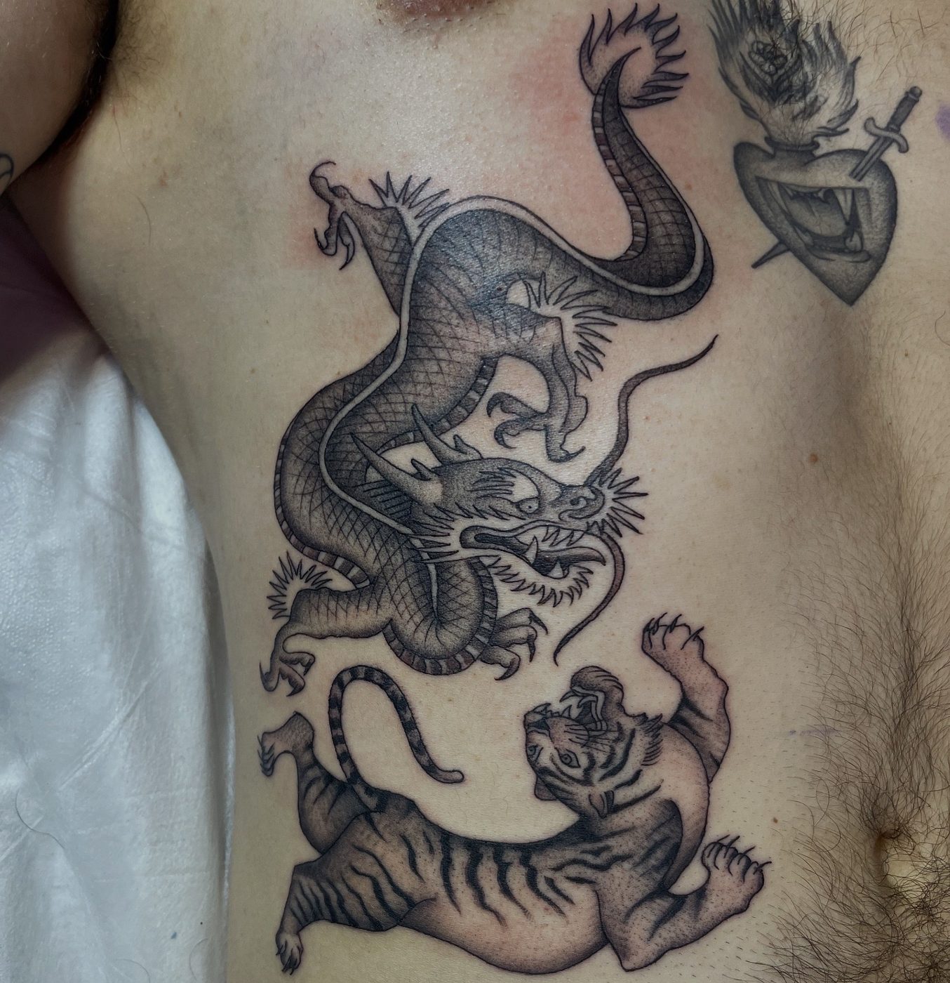 Large black and grey stomach tattoo of a coiling dragon above a roaring tiger